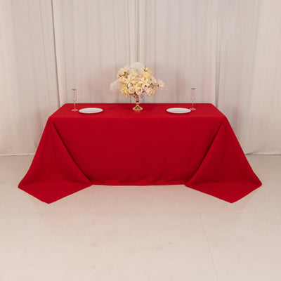 Red tablecloth with decorative floral arrangement and dinner plates.