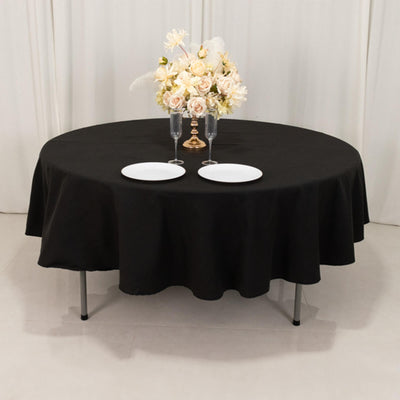 Round black tablecloth with plates and elegant floral arrangement.