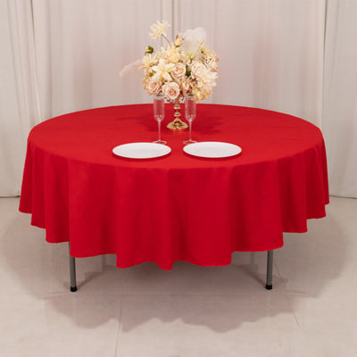 Round red tablecloth draped over a table set with plates and glasses.