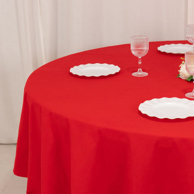 Red tablecloth with white plates and glasses on a round dining table.