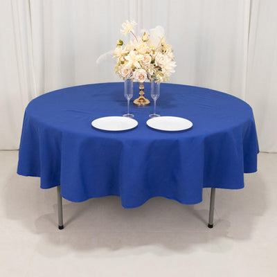 Round blue tablecloth on a table set with plates and a floral centerpiece.