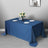 Blue tablecloth draped over a table with plates and a vase of flowers.