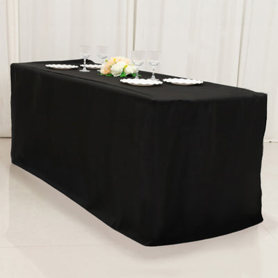 Black tablecloth draped over a rectangular table with plates and glasses set on top.