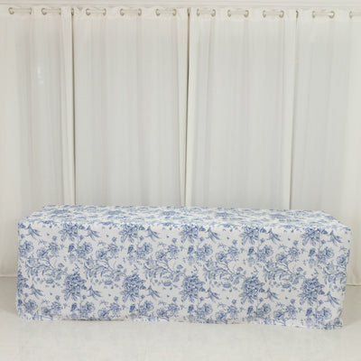Floral patterned tablecloth draped over a table against white curtains.
