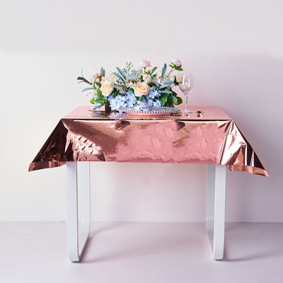 Rose gold tablecloth on a white table with floral arrangement and glassware.
