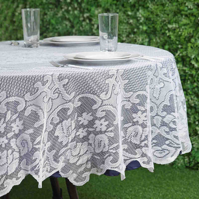 Lace tablecloth draped over a round table with clear glasses and plates.