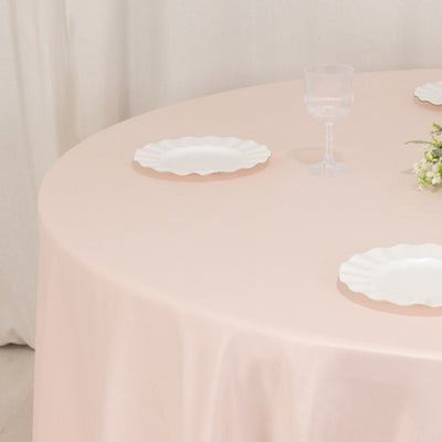 Elegant pink tablecloth with white plates and glassware on a round table.