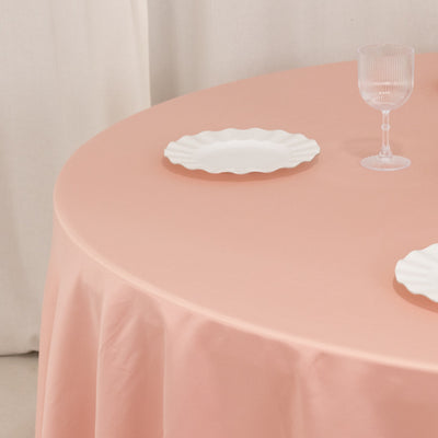 Round pink tablecloth with white plates and glass on a clean surface.