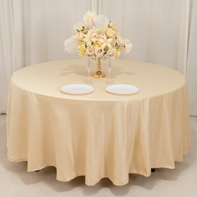 Elegant round table set with a beige tablecloth and floral centerpiece.