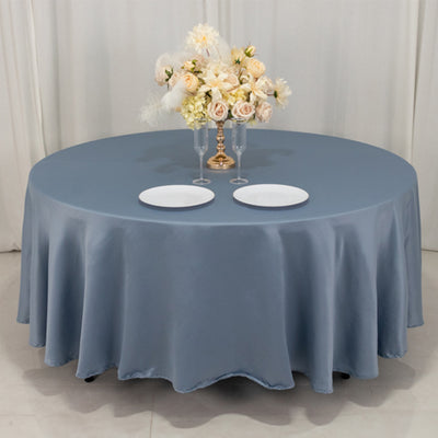 Round blue tablecloth with floral arrangement and plates on a table.