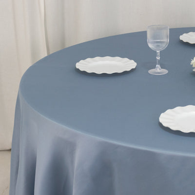 Blue tablecloth with white plates and glass on a round table.