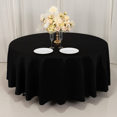 Black round tablecloth draped over a table set with plates and floral centerpiece.