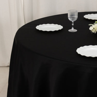 Black tablecloth with white plates and glass on a round table setting.