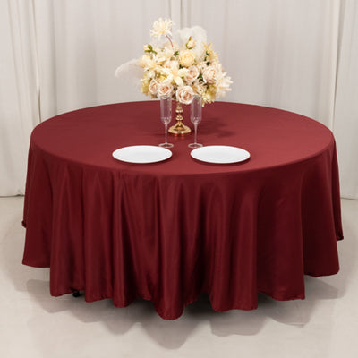 Round burgundy tablecloth with floral centerpiece and plates on a styled table.