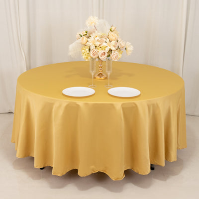 Round gold tablecloth draped over a table with plates and floral centerpiece.