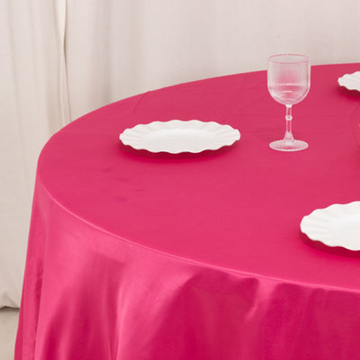 Pink tablecloth with white plates and a glass on a round table.
