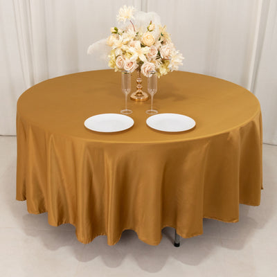 Round gold tablecloth draped over a table with plates and floral centerpiece.