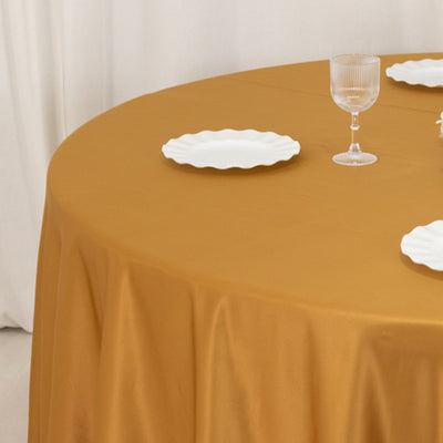 Golden round tablecloth draped on a table with white plates and a glass.