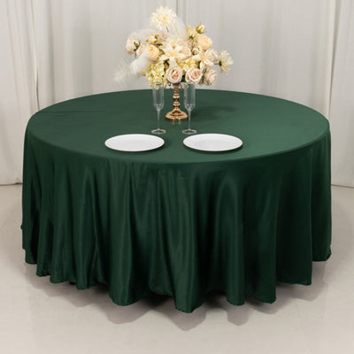 Green round tablecloth draped on a table with plates and floral centerpiece.