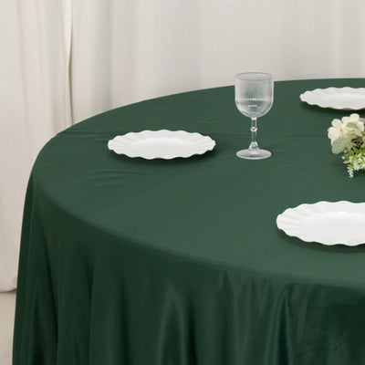 Green tablecloth with white plates and a glass on a round table.