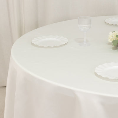 Round table set with white plates and a glass on a white tablecloth.