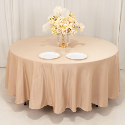 Round beige tablecloth with floral centerpiece and white plates on a table.