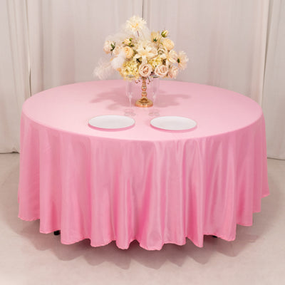 Pink tablecloth on a round table with floral centerpiece and empty plates.