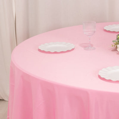 Pink tablecloth draped over a round table with white plates and a glass.