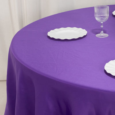 Purple tablecloth with white plates and glassware on a round table.