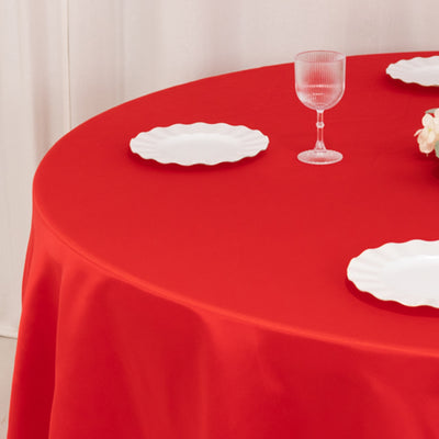 Red tablecloth with white plates and glass on a round table.