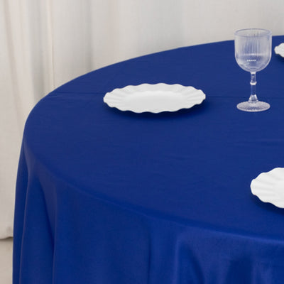 Blue tablecloth with white plates and glass on a round table.
