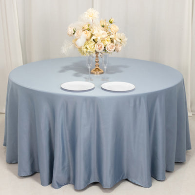 Round table with a blue tablecloth, two white plates, and floral centerpiece.