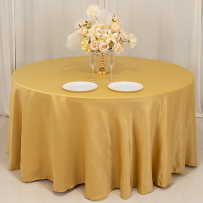 Round table with gold satin tablecloth and floral centerpiece.