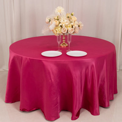 Round pink satin tablecloth with plates and a floral centerpiece.