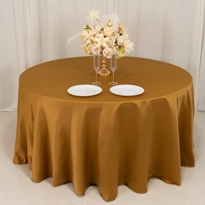 Round gold tablecloth on a dining table with floral centerpiece and plates.