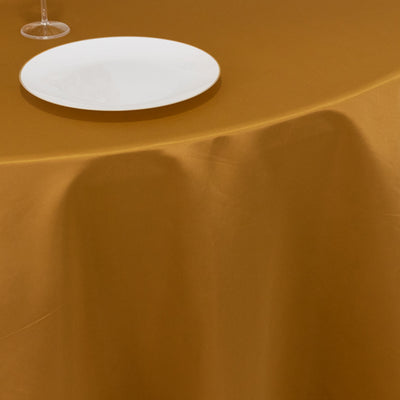 White plate on a golden tablecloth with a glass beside it.