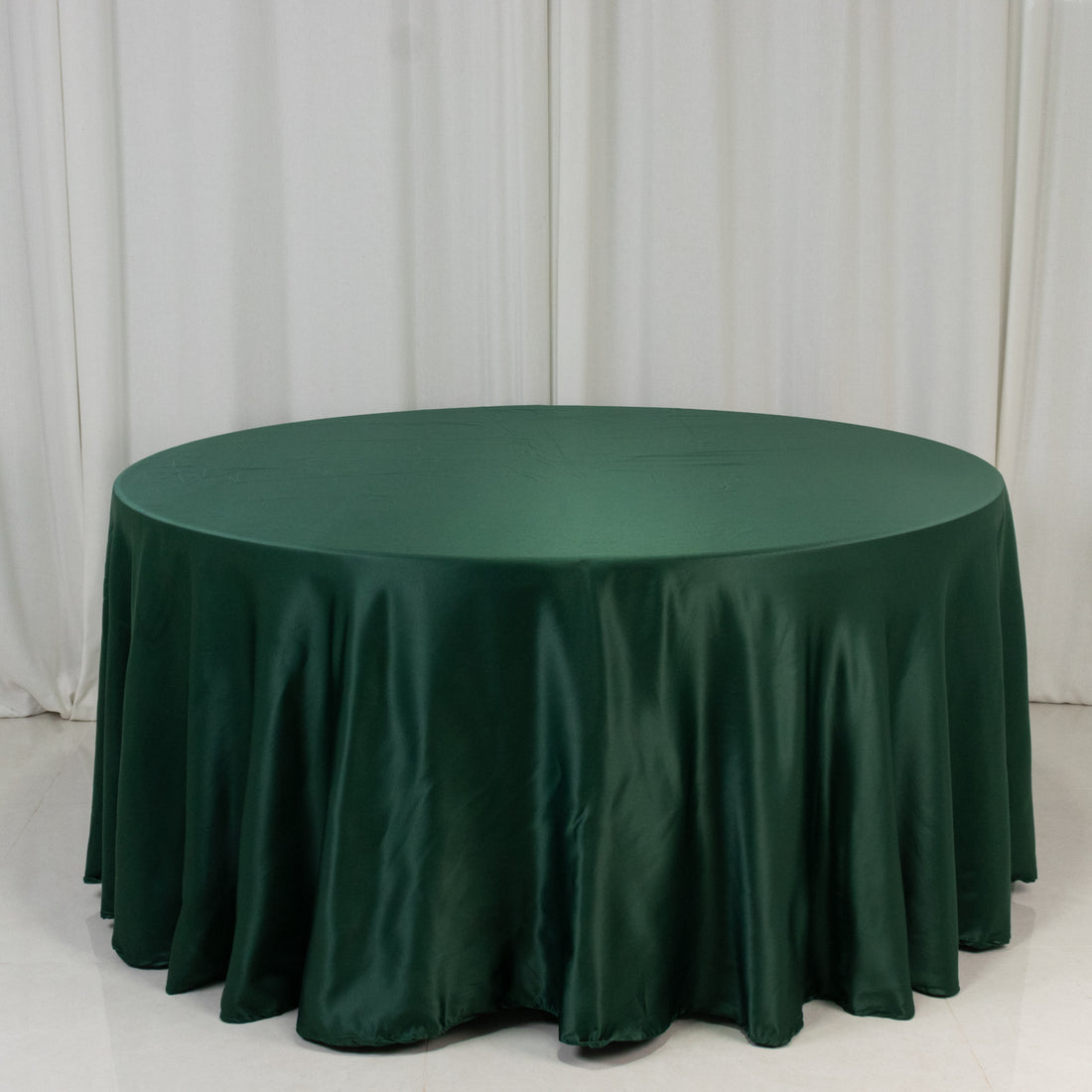 Green satin tablecloth draped over a round table in a studio setting.
