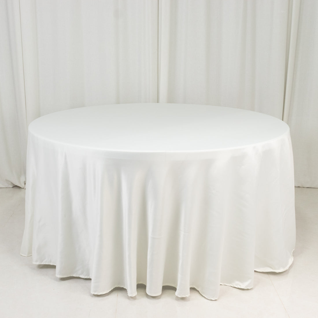 Round white table with a smooth tablecloth on a plain backdrop.