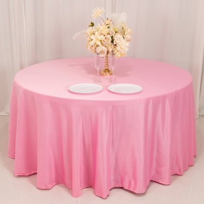 Round pink tablecloth draped over a table with plates and a floral centerpiece.