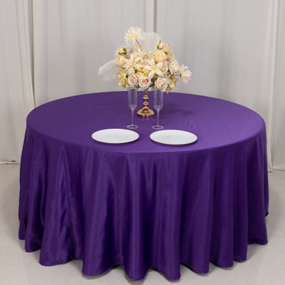 Purple tablecloth with elegant floral arrangement and two plates set on a round table.