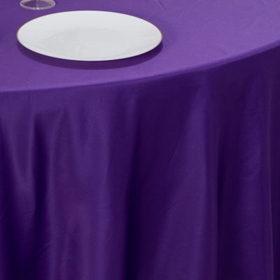 Purple tablecloth with white plate and glass on a dining table.