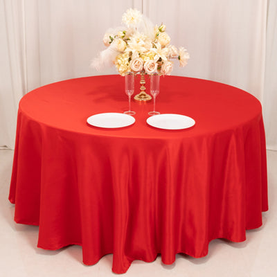 Red round table with elegant floral centerpiece and two white plates.