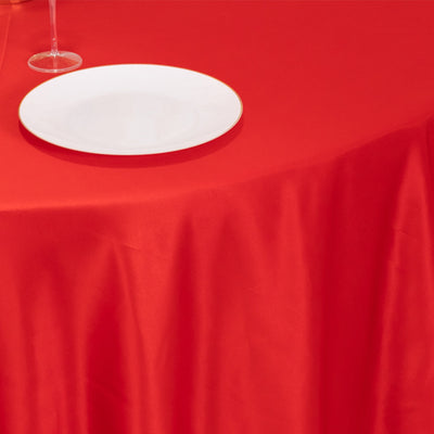 Red tablecloth with a white plate and wine glass set on a dining table.