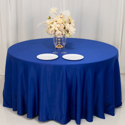 Round blue tablecloth draped over a table with floral centerpiece and plates.