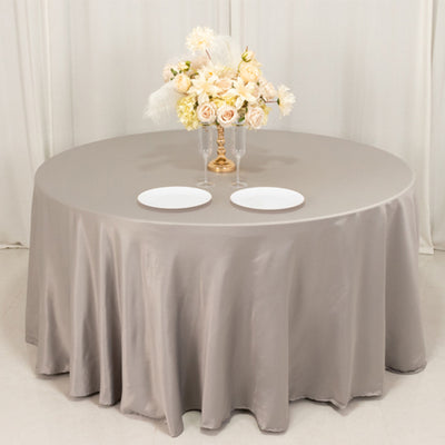 Elegant round table with a gray satin tablecloth, floral centerpiece, and plates.