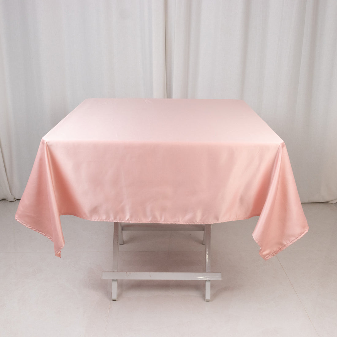 Pink satin tablecloth on a folding table in a studio setting.