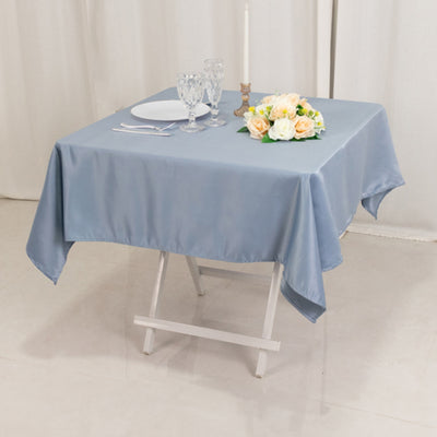Blue satin tablecloth draped over a folding table with elegant tableware and flowers.