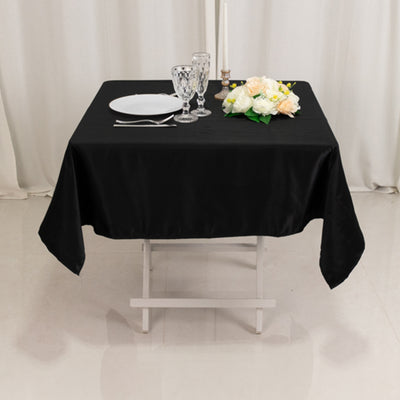 Elegant black tablecloth with dining setup featuring plates, glasses, and floral arrangement.