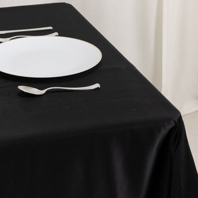 Elegant black tablecloth with white plate and silver cutlery arranged neatly.