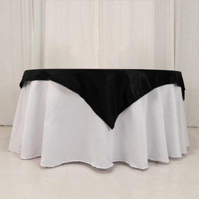 Round table with a black satin tablecloth draped over a white table cover